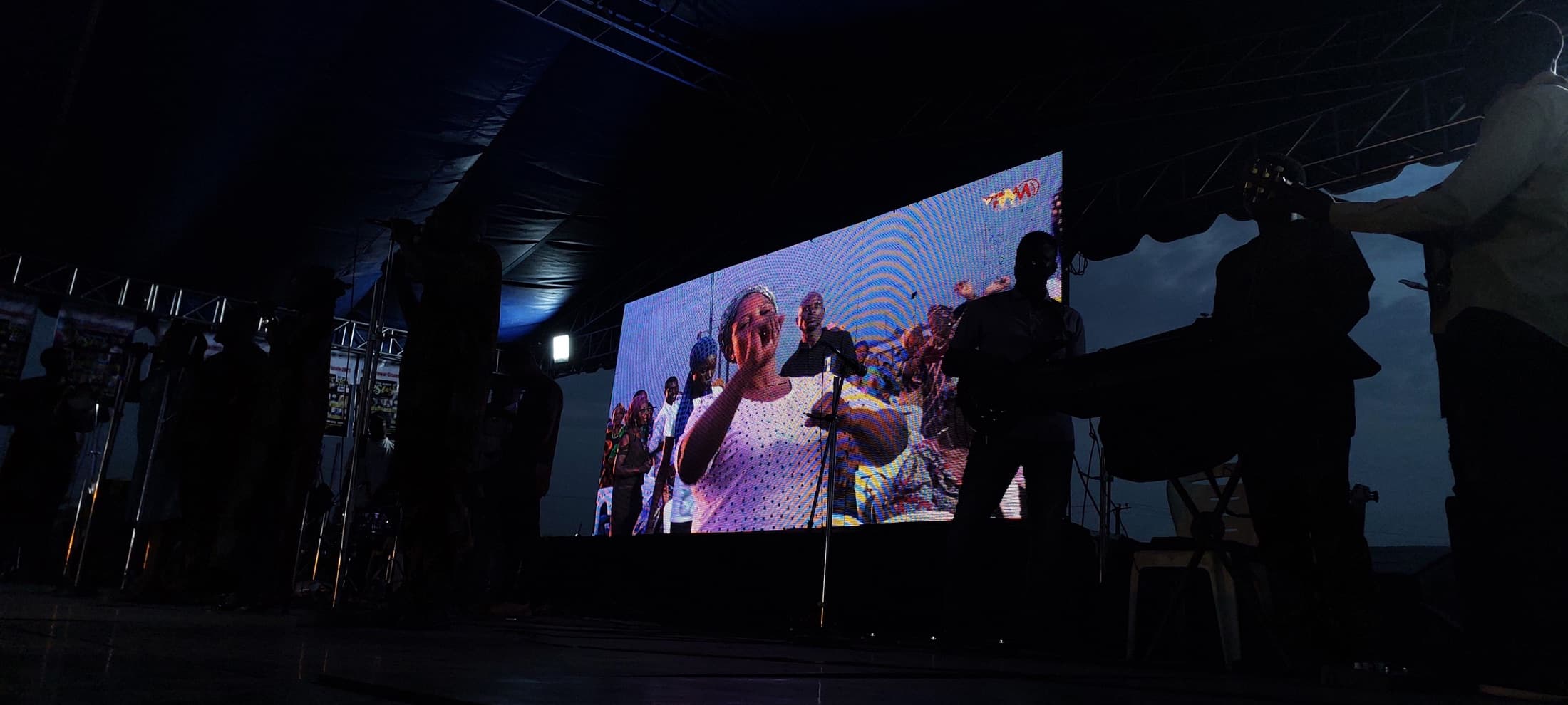 A large LED screen showing a live broadcast at a night-time outdoor event